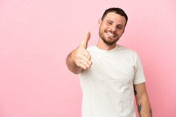 Young Brazilian man isolated on pink background shaking hands for closing a good deal