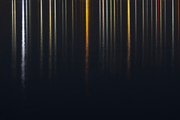 Colorful seaside evening lights reflection, vertical lines on dark background; color photo.