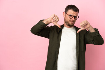 Young Brazilian man isolated on pink background showing thumb down with two hands