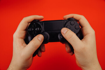 Young man holds a game controller isolated on red background. Cybersport or gaming concept