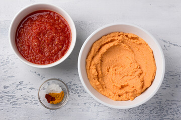 Ingredients for homemade lentil pancakes: fresh tomato sauce with spices, ground red lentils and spices (turmeric, paprika, salt) on a light gray background