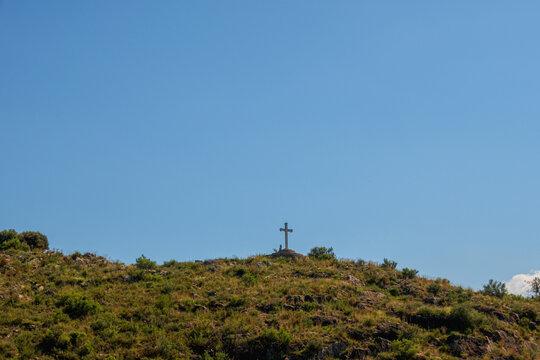 Small cross on top of a hill with blue sky in the background.