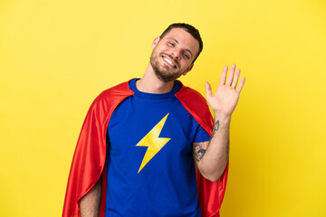 Super Hero Brazilian man isolated on yellow background saluting with hand with happy expression © luismolinero