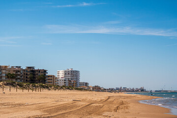 Daimuz beach, with clean and fine sand, on a sunny afternoon, with the port of Gandia in the background.
