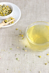 Chamomile herbal tea in glass cup and jar with dry herb flowers, above overhead view, naturopathy, natural medicine, healing drinks for sleep, skin and hair care concept