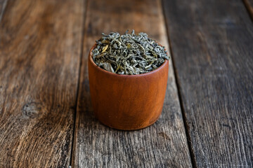 Dry green tea leaves in a wooden cup, on an old oak table. Style "wabi sabi", "modest simplicity", "unassuming simplicity", "touch of antiquity; pacification of loneliness ”.
