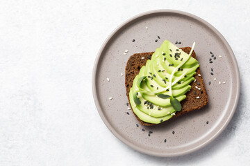 Whole grain rye bread toast with sliced avocado on white stone table background. Healthy avocado open sandwich for breakfast or lunch. Flat lay, top view, copy space	