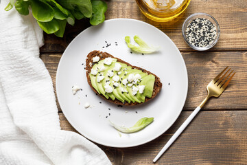 Whole grain rye bread toast with goat cheese and avocado on wooden table background. Healthy...