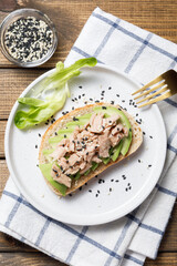 Avocado, canned tuna toast on wooden table background. Healthy food, avocado open sandwich for breakfast or lunch. Flat lay, top view