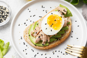 Avocado, canned tuna and boiled egg toast on white stone table background. Healthy food, avocado open sandwich for breakfast or lunch. Flat lay, top view, close up