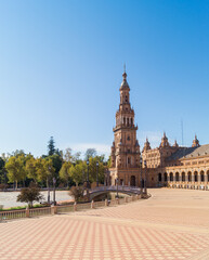 Fototapeta na wymiar North tower of the Plaza de Espana in Seville (Andalusia, Spain). View of the square and the pedestrian bridge that crosses the estuary. Emblematic monumental building and main tourist attraction.