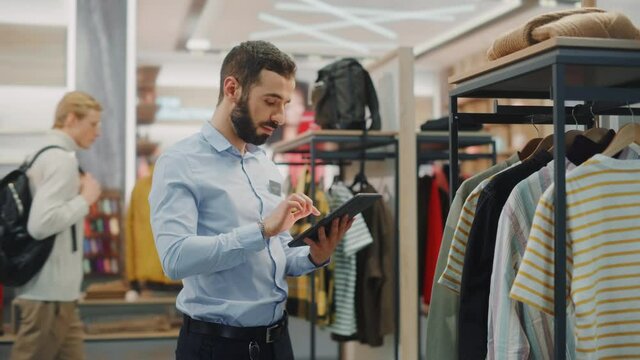 Clothing Store: Male Visual Merchandising Professional Uses Tablet Computer To Create Collection. Fashionable Shop Sales Retail Manager Checks Stock. Small Business Owner Orders Stylish Items