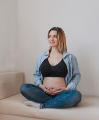 A beautiful pregnant woman is sitting on the sofa smiling and looking out the window.