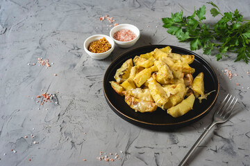 Delicious lunch: potato slices baked with cheese. Potatoes with cheese on a black plate on a gray background