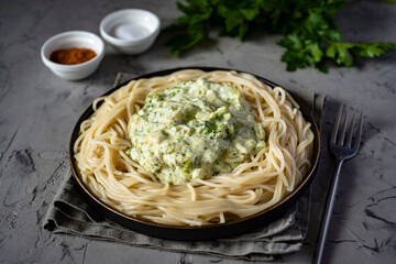 Spicy pasta with broccoli and cream sauce on a black plate on a gray background. Spaghetti for lunch