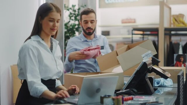 Clothing Store Checkout Cashier Counter: Female and Male Retail Sales Managers Carefully Packing Online Ordered Clothes into Boxes. Fashionable Shop, with Stylish Brand Designs Available on Internet