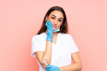 Woman dentist holding tools isolated on pink background unhappy and frustrated