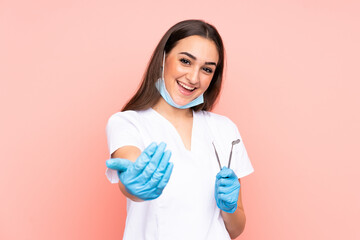 Woman dentist holding tools isolated on pink background inviting to come - obrazy, fototapety, plakaty
