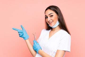 Woman dentist holding tools isolated on pink background pointing finger to the side