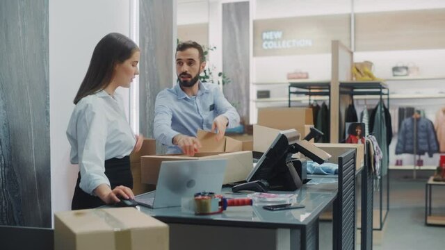Clothing Store Checkout Cashier Counter: Female and Male Retail Sales Managers Carefully Packing Online Ordered Clothes into Boxes. Fashionable Shop, with Stylish Brand Designs Available on Internet