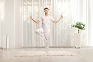 Young man standing in a yoga pose with one lifted leg in a room