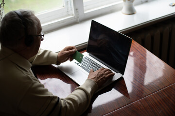 Smiling senior man wear earphones wave to camera having video call on laptop, happy elderly male in headphones sit on couch at home talk using modern technologies and wireless connection