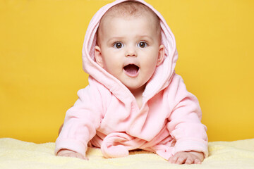 Adorable baby in pink bathrobe on bright yellow background. Free space for text. Child looking at...