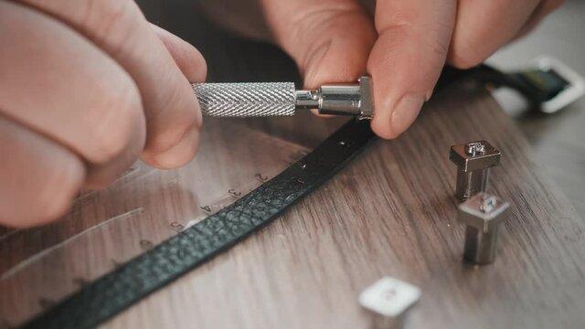 close up of man hand puts on stamp on instrument to punch letters on leather bracelet. Making leather accessories