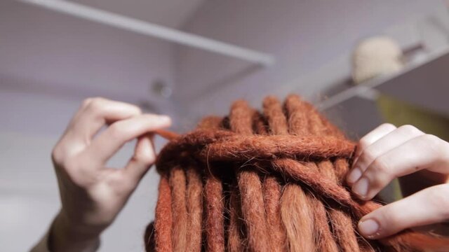 A young girl with red dreadlocks looks in the mirror and Ties dreadlocks, in bathroom in the morning getting ready during everyday routine at home