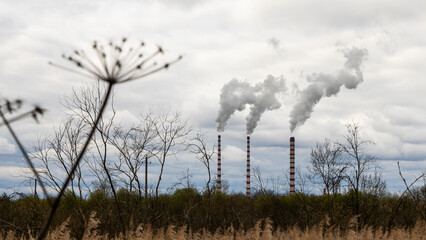 Industrial smoke from chimney on dramatic sky background. View of high chimney pipes with grey smoke from coal power plant. Production of electricity with fossil fuel. Wind blowing pollution.