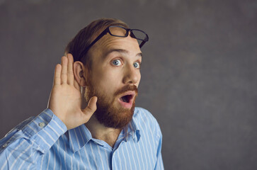 Omg I can hear them chat about something interesting. Man isolated on gray background puts hand to...