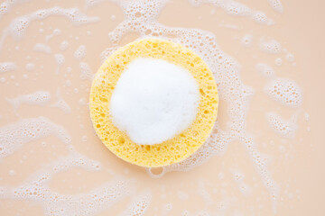 Natural beige cosmetic sponge with cleansing foam on pastel background. Morning or evening beauty routine. Beauty care for face concept. Top view