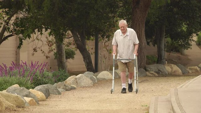 Wide shot of senior man (82 year old Caucasian) walking in the park using a walker