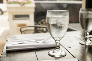 A water glass and a silverware setting on a wood table at a high end restaurant