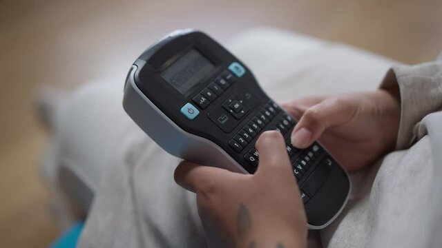 Close-up of tattooed female African American hands typing Remote working on label maker. Unrecognizable young woman in home office on coronavirus isolation