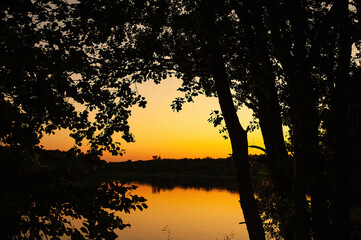 Beautiful orange sunset on the lake framed by black silhouettes of trees