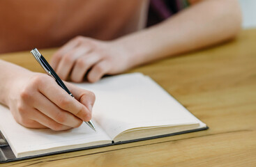 Close-up of a student's hand holding a pen and making notes in a notebook