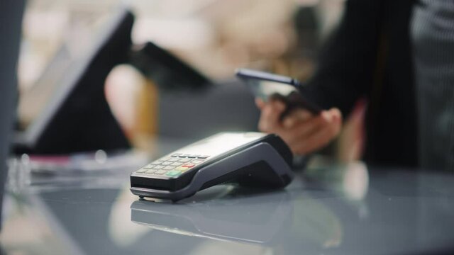 Clothing Store: Woman At Counter Buys Clothes Paying with Smartphone Through, Contactless NFC Terminal. Department Store, Shopping Center, Mall Purchase. Close-up Focus on Mobile Phone
