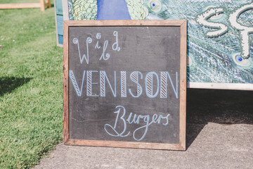 Hand written blackboard saying wild venison burgers outside at a catering van