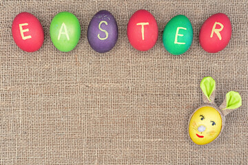 Yellow egg in the shape of an Easter bunny and multicolored eggs with the inscription 