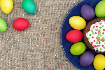 Round plate with multicolored Easter eggs and Easter cake on a burlap background.