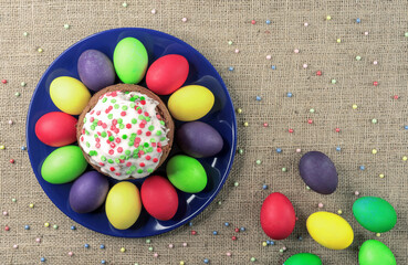 Round plate with multicolored Easter eggs and Easter cake on a burlap background.