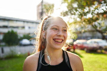 a beautiful red-haired girl with green eyes in the foreground smiles and looks forward in a park near the city in a sunset