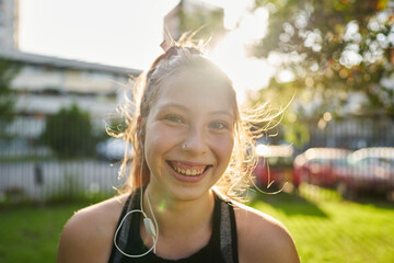 a beautiful red-haired girl with green eyes in the foreground smiles and looks forward in a park near the city in a sunset