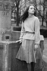 Black and white melancholic portrait of a woman. Young girl. A brunette in a sweater and dress looks into the camera