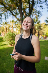 a beautiful red-haired girl with green eyes in a medium shot stretches her muscles to be able to start playing a sport in a park in the center of the city