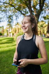 a beautiful red-haired girl with green eyes in a medium shot stretches her muscles to be able to start playing a sport in a park in the center of the city