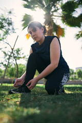   A beautiful white woman with brown hair and a sports outfit fastens the laces of her sneakers before exercising in a park near the city of Santiago de Chile