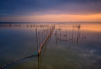 typical fishing system with rods and sticks, of the Valencia lagoon in Spain. Nice image with some very interesting lines. Close to sunset time with an impressive cloudy sky and beautiful colors.