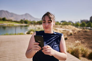 A beautiful white woman with brown hair and a sports suit takes a selfie exercising and listening to music in a park in the city center